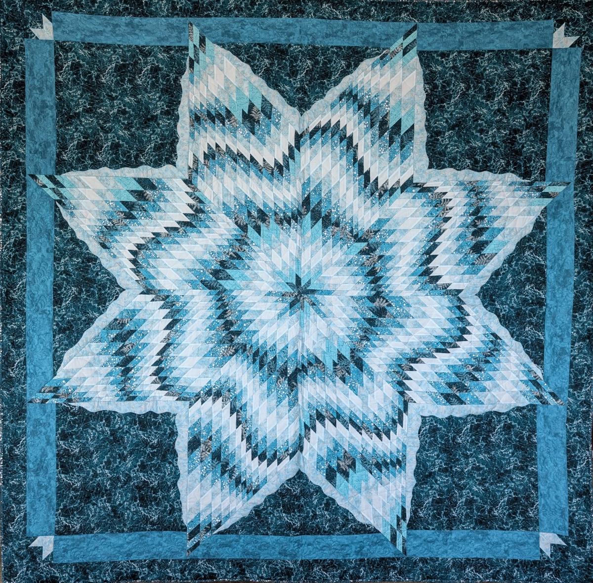 A quilt with blue and green colours and the shape of an 8-point star.